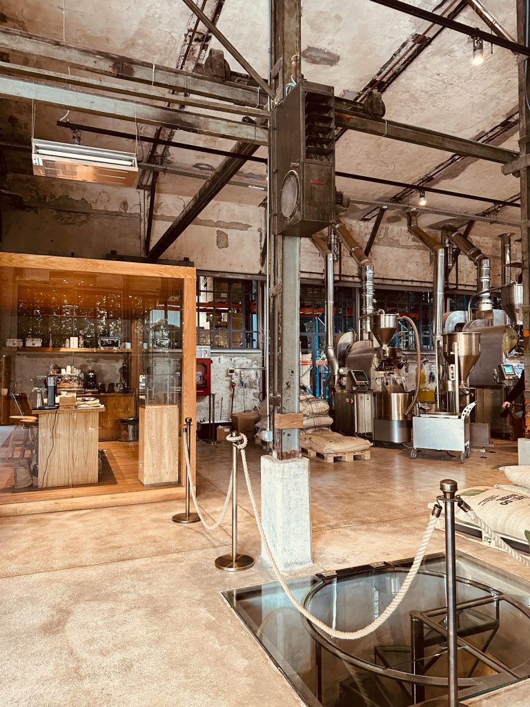 A spacious industrial coffee production facility with machinery and a tasting booth.