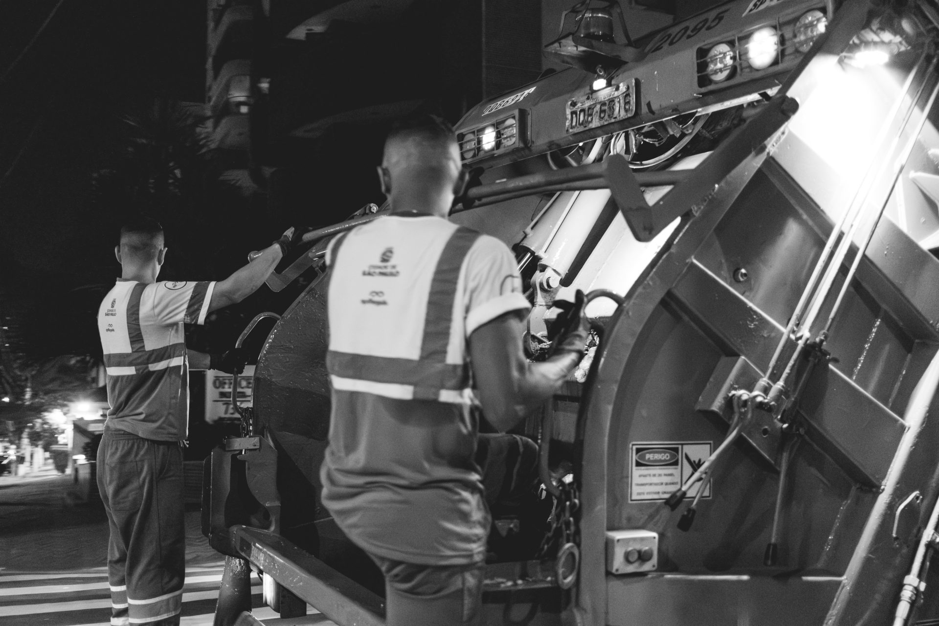 Garbage men are working, emptying the trash truck.